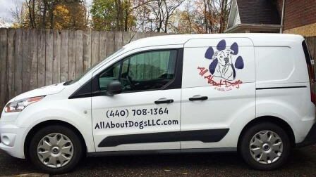 A white van with the words " all about dogs llc " written on it.