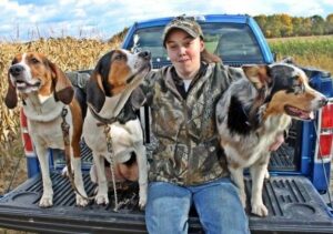 A woman standing in the back of a truck with dogs.