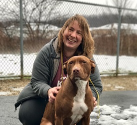 A woman kneeling down next to a brown and white dog.