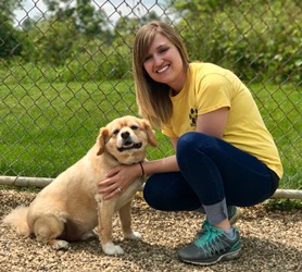 A woman kneeling down next to a dog.