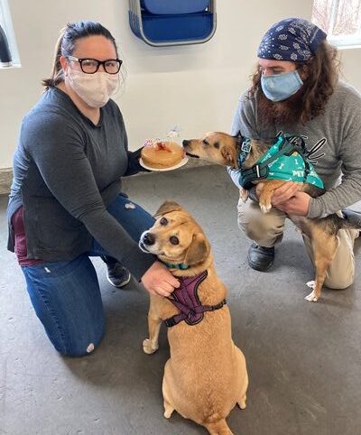 Two women and a dog are sitting in front of some food.